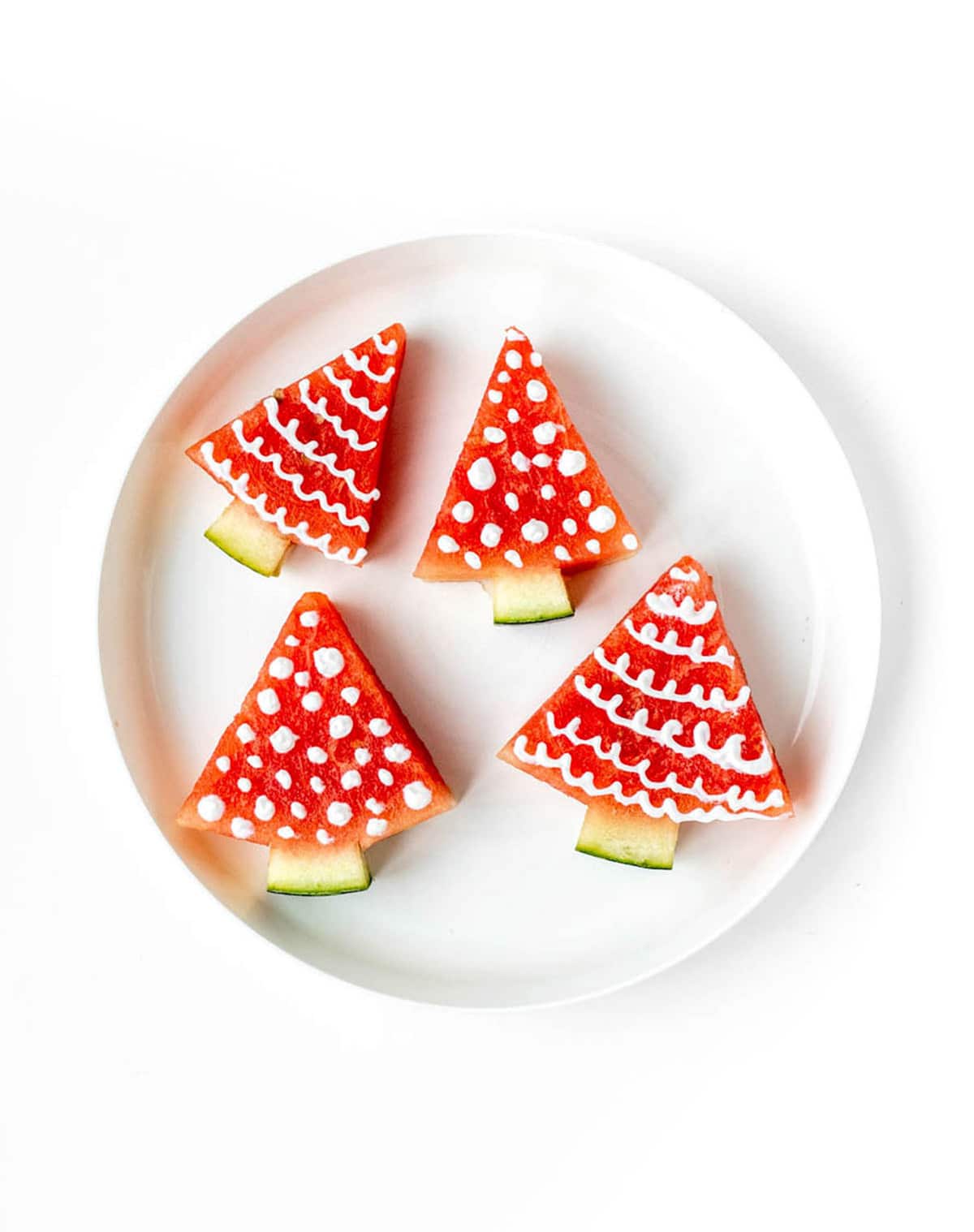 Four watermelon Christmas trees on a white plate.