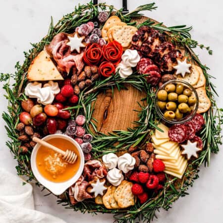 A holiday charcuterie wreath board filled with meats, cheeses, crackers, fruit, honey and goodies.