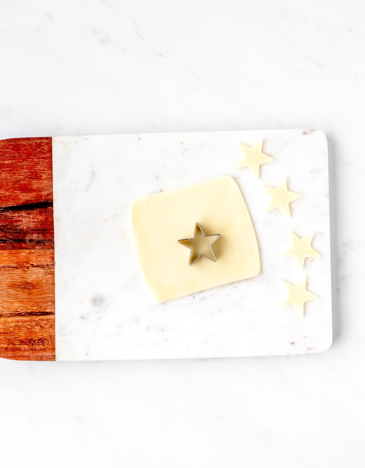 Making mini stars out of a piece of cheese using the mini star cutter, on a cutting board.