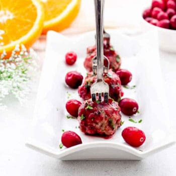 Cranberry chicken meatballs on a serving tray with little forks poked into them.