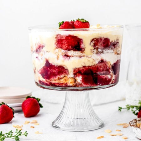 English trifle recipe with custard, sponge cake and jam in a fotted trifle bowl topped with strawberries.