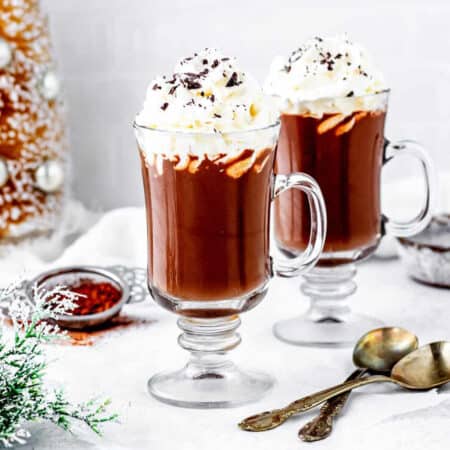 Two cups of cacao hot chocolate topped with whipped cream.
