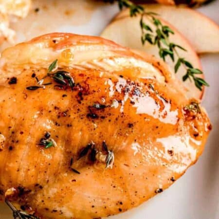 Apple and brie stuffed chicken on a white tray with fresh thyme.