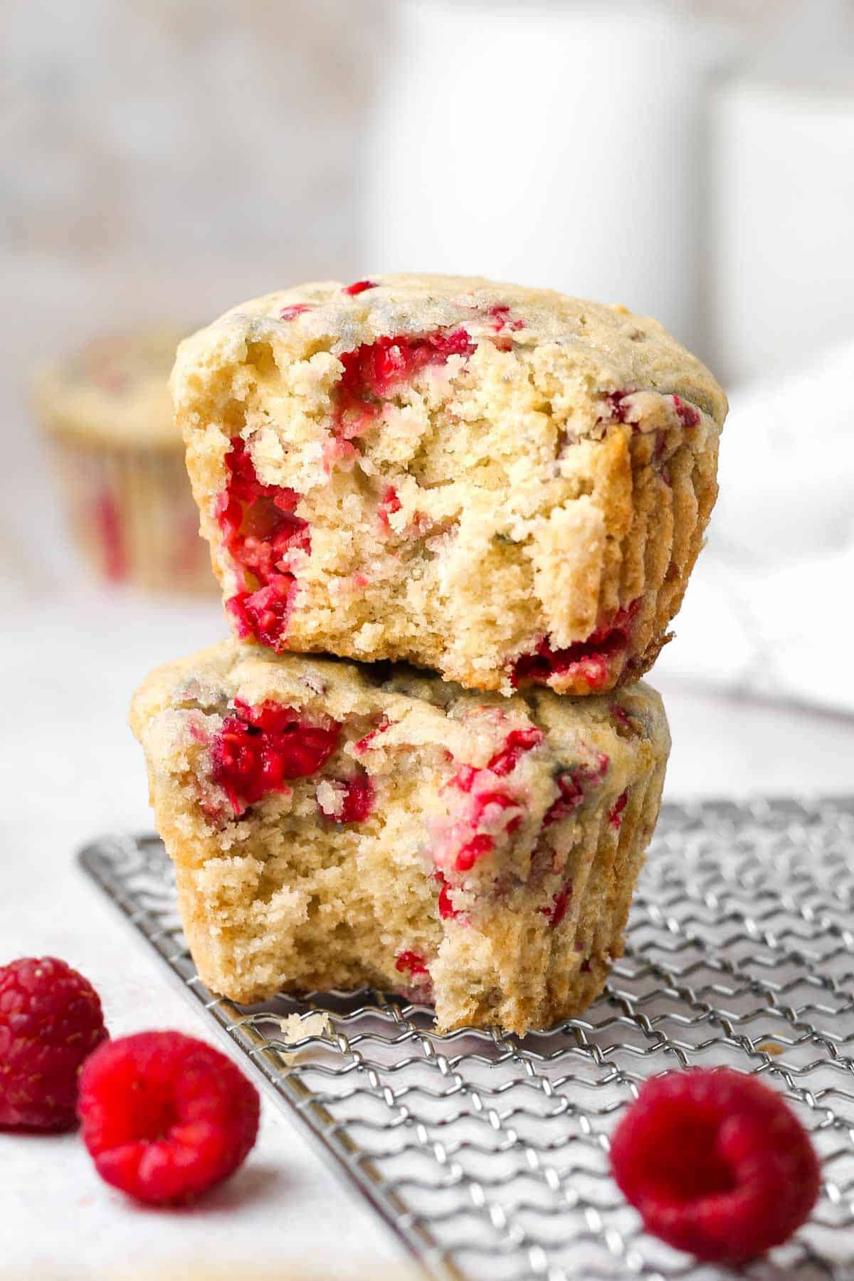 A close-up of two half-bitten healthy vegan raspberry muffins sitting on top of one another on a cooling rack.