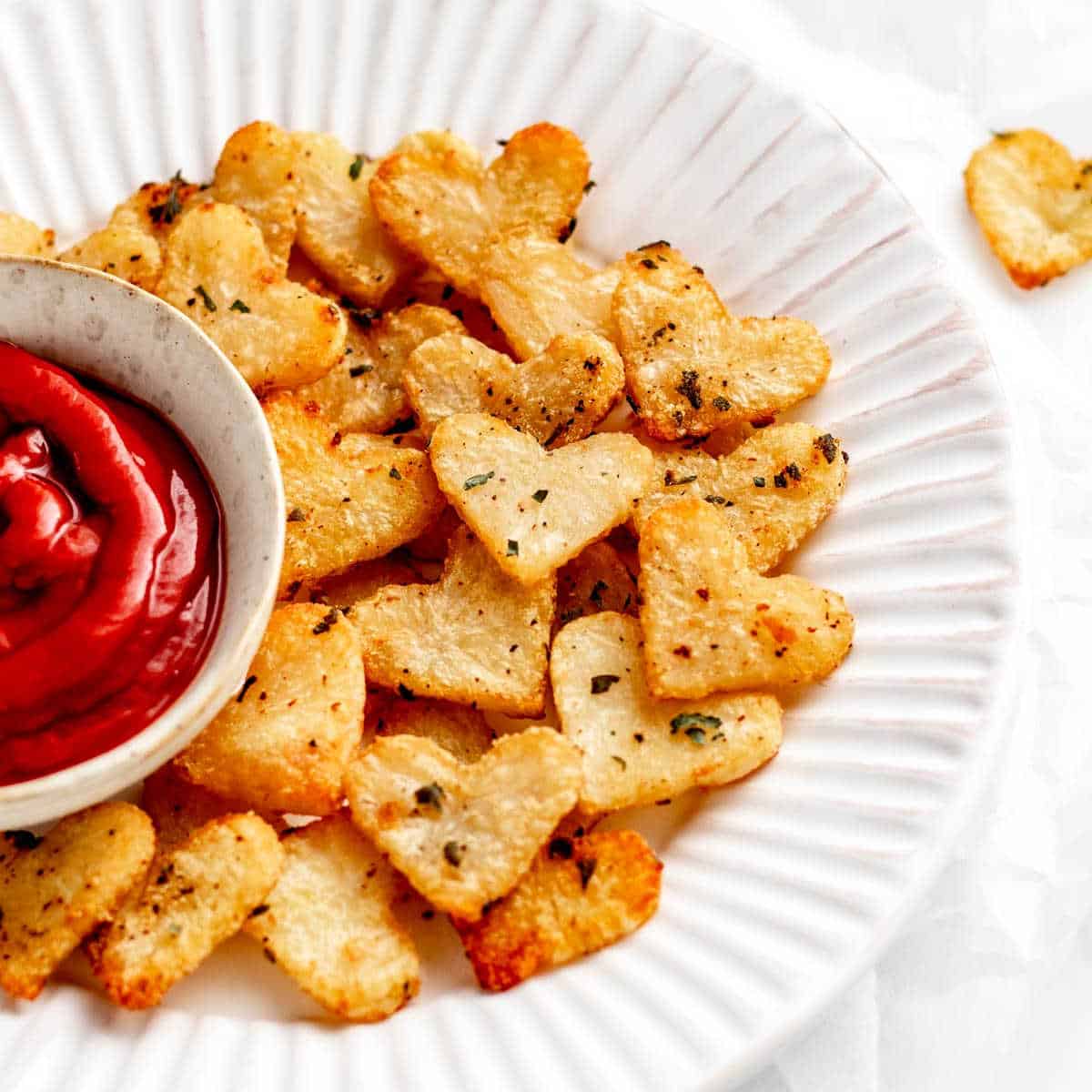 Roasted heart potatoes on a white plate with a small bowl of ketchup.