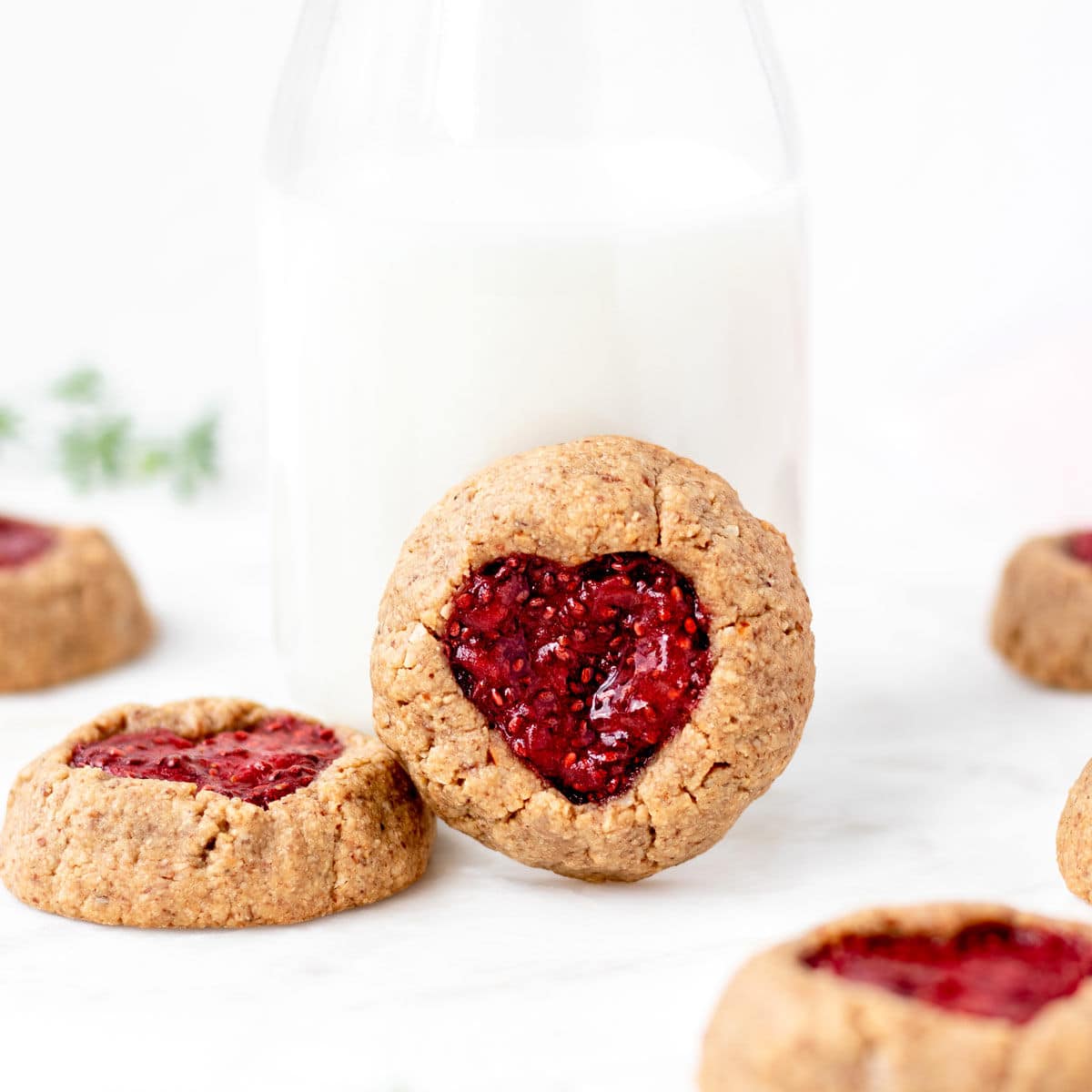Heart cookies with jam resting up against a glass milk jug.