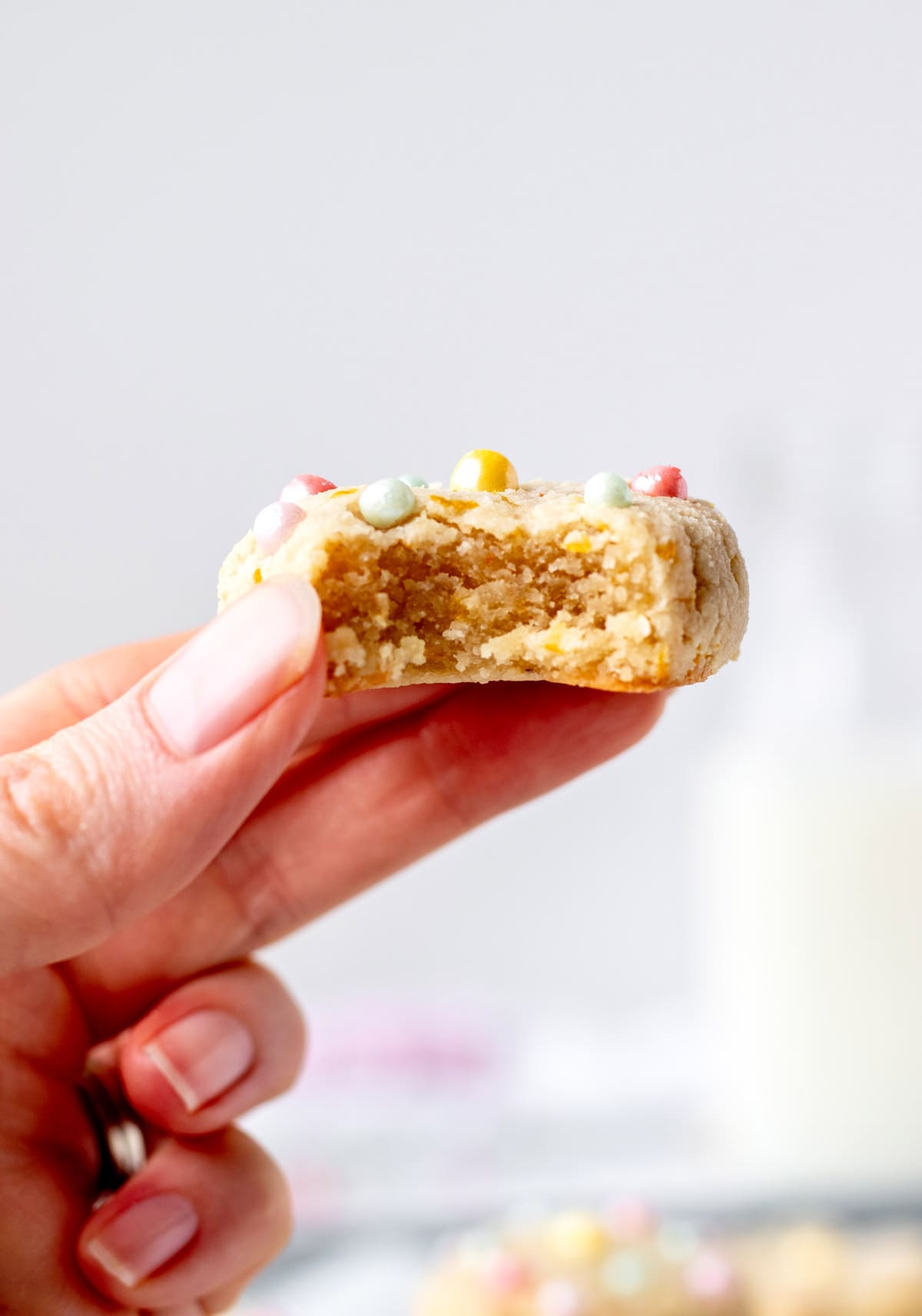 A hand holding up a vegan lemon cookie with a bite taken out of it.