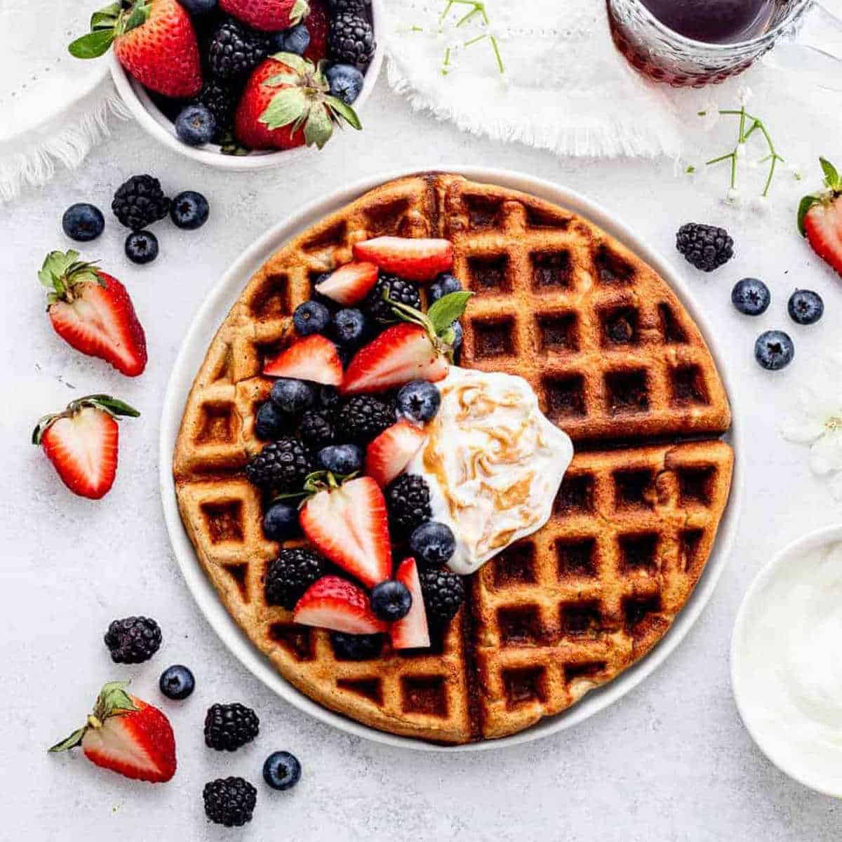 A banana oatmeal waffle on a plate with mixed berries and yogurt.