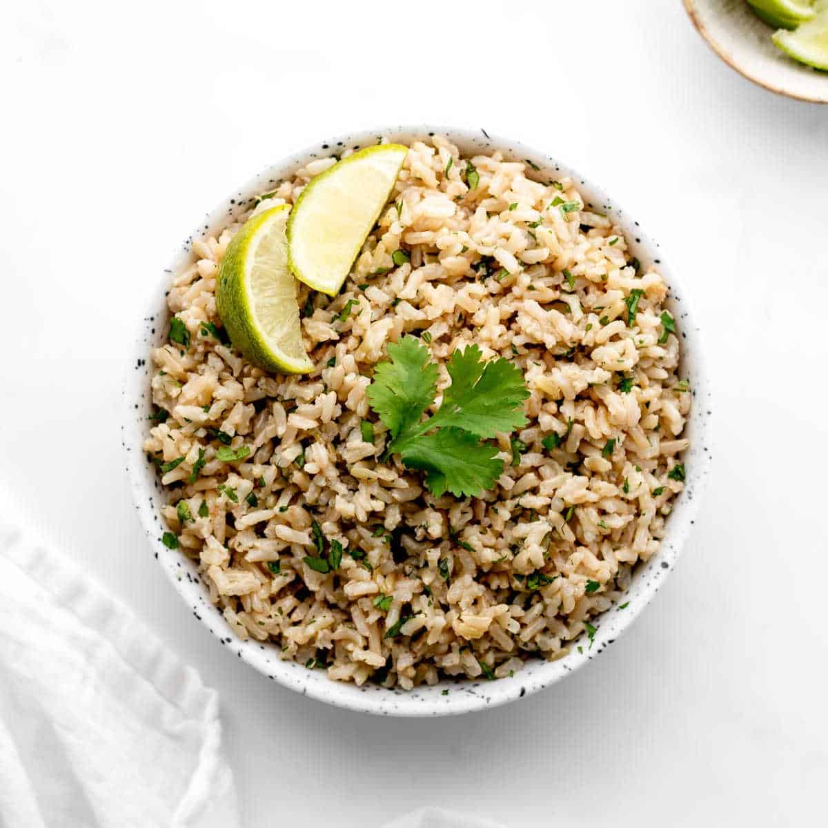 Coconut lime rice in a bowl topped with cilantro and lime wedges.