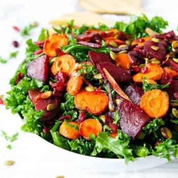 Kale beet salad with roasted carrots, shallots and pumpkin seeds in a white bowl.