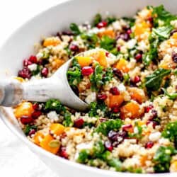 A serving spoon digging into a large bowl of pomegranate quinoa salad.