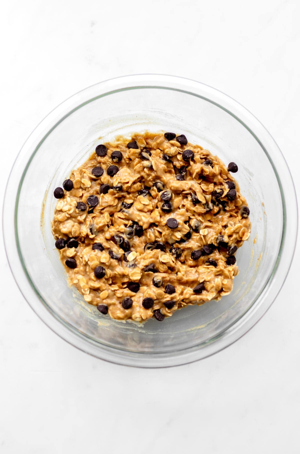 Chocolate chips added to the cookie mixture in a glass bowl.