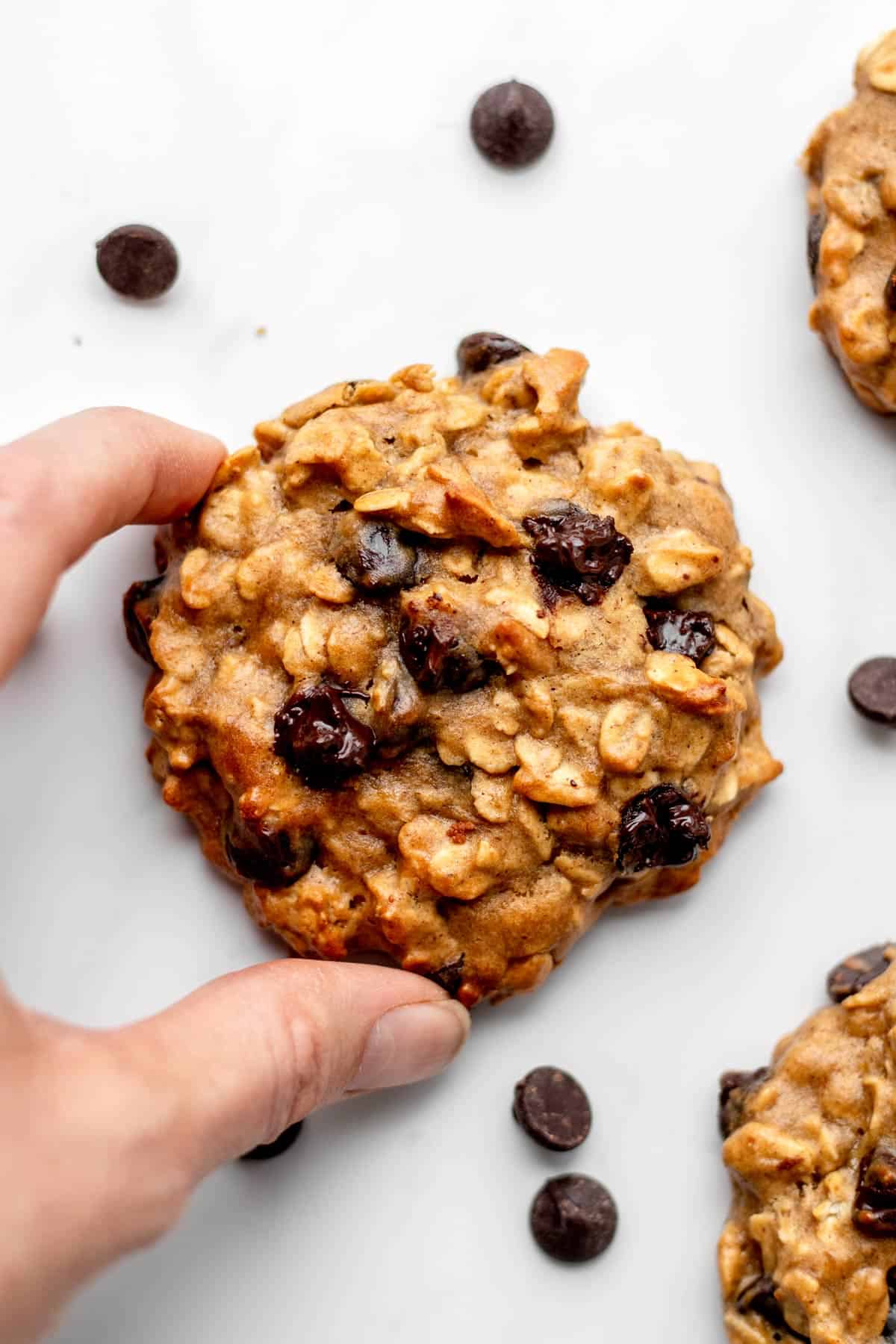 A hand picking up a banana protein cookie off the counter.