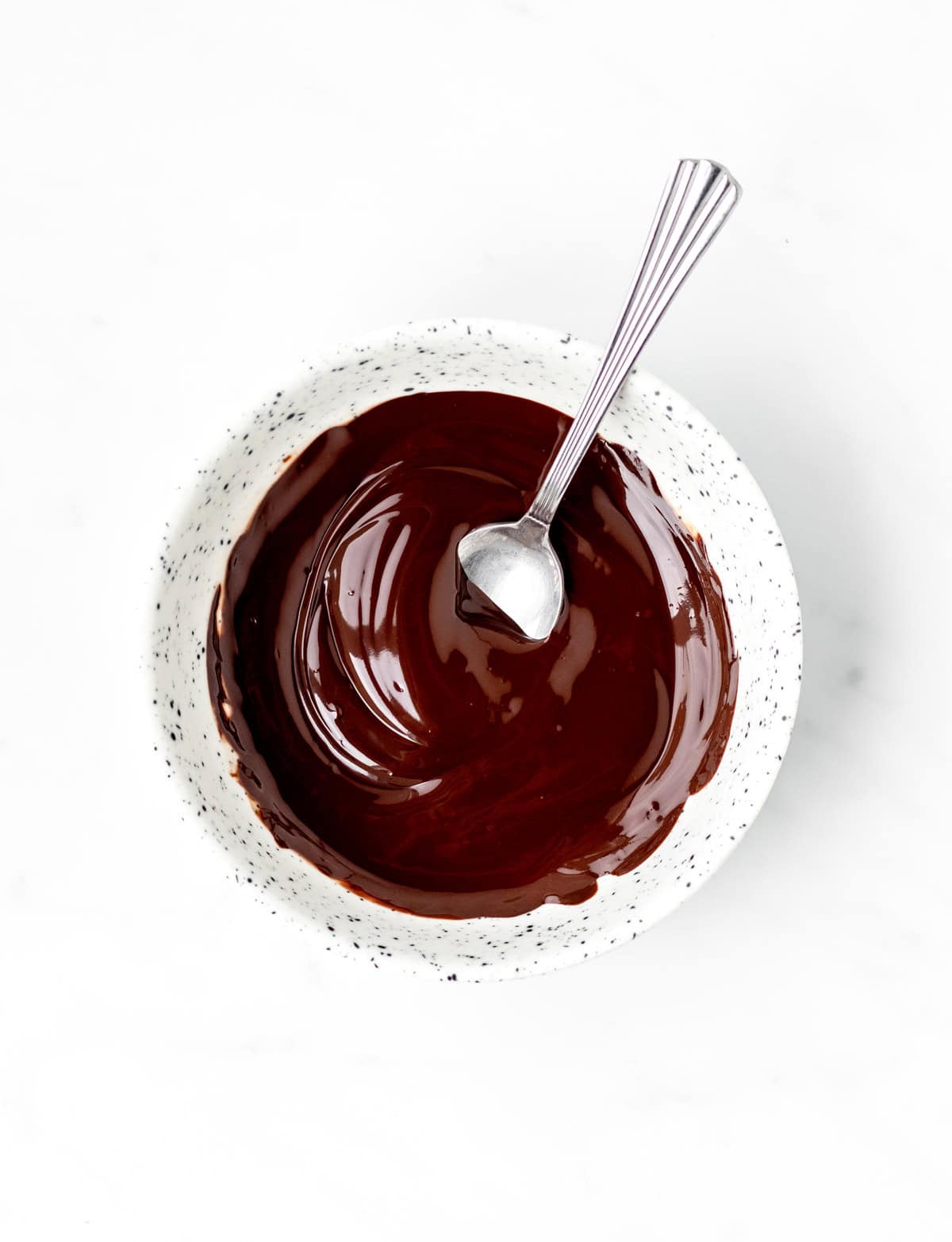 A spoon stirring some melted chocolate in a bowl.