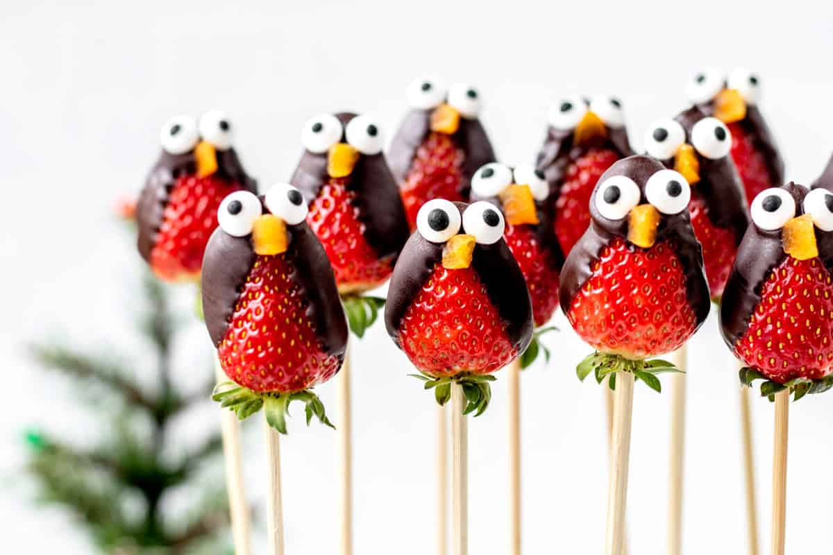 A group of strawberry penguins on wooden sticks.