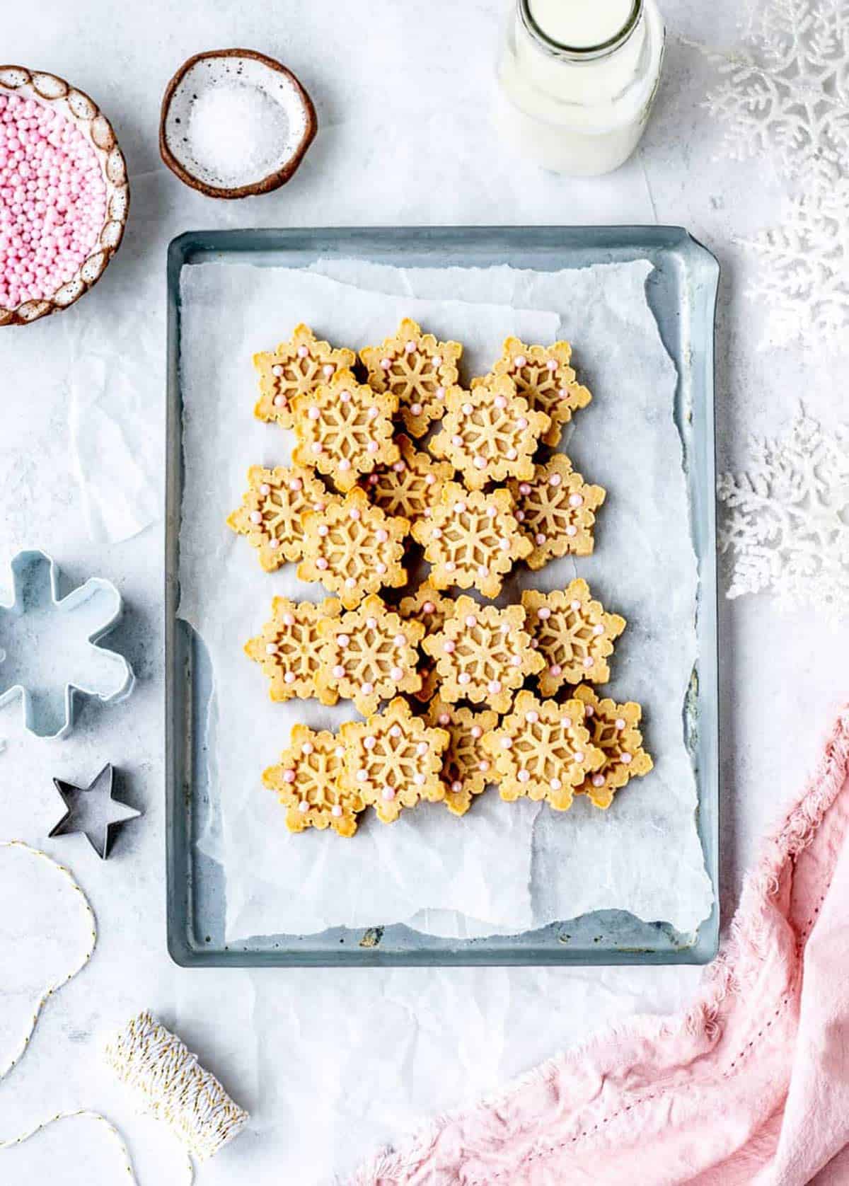 Bird's eye view of snowflake shaped almond flour shortbread cookies piled on a baking tray.