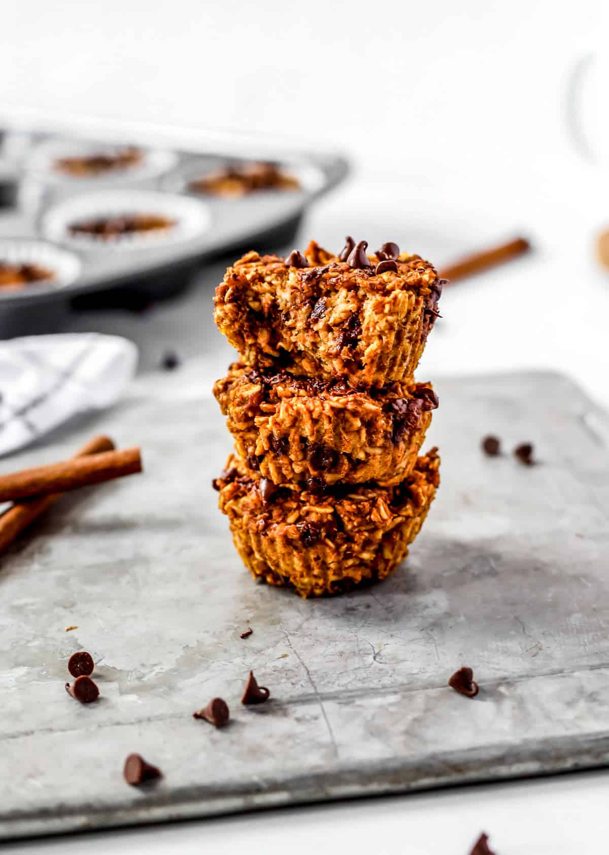 Three pumpkin oatmeal muffins stacked on top of each other with a bite taken out of the top one.