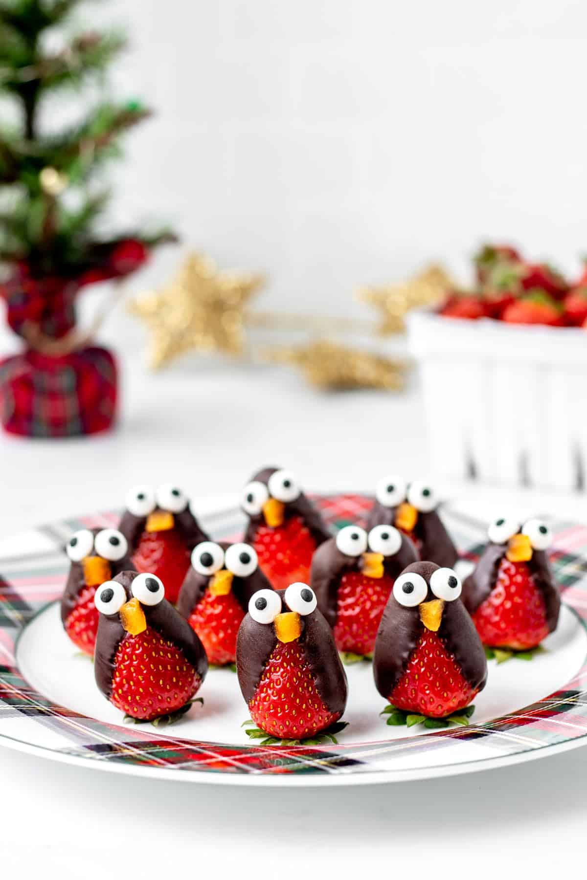 A group of chocolate covered strawberry penguins on a checkered plate.