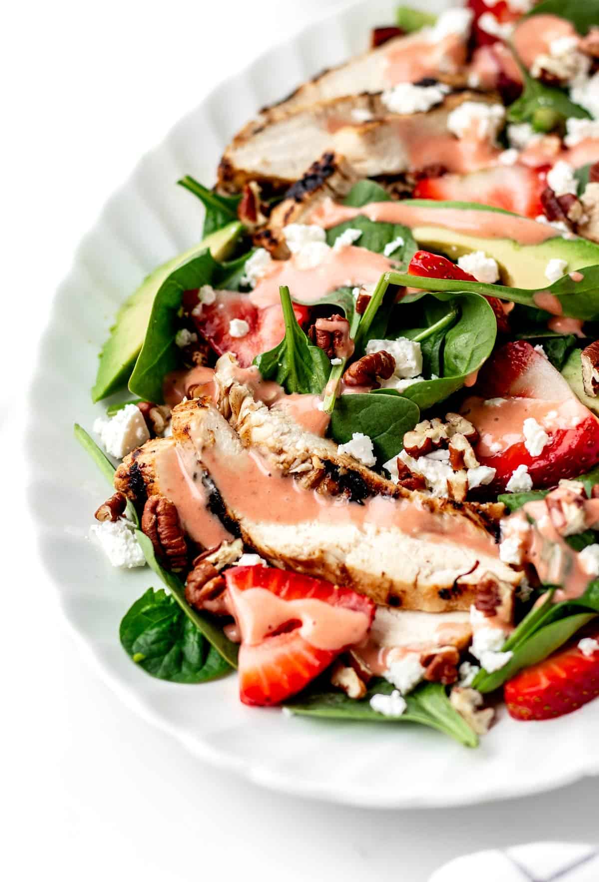Grilled chicken spinach salad on a tray drizzled with strawberry vinaigrette dressing.