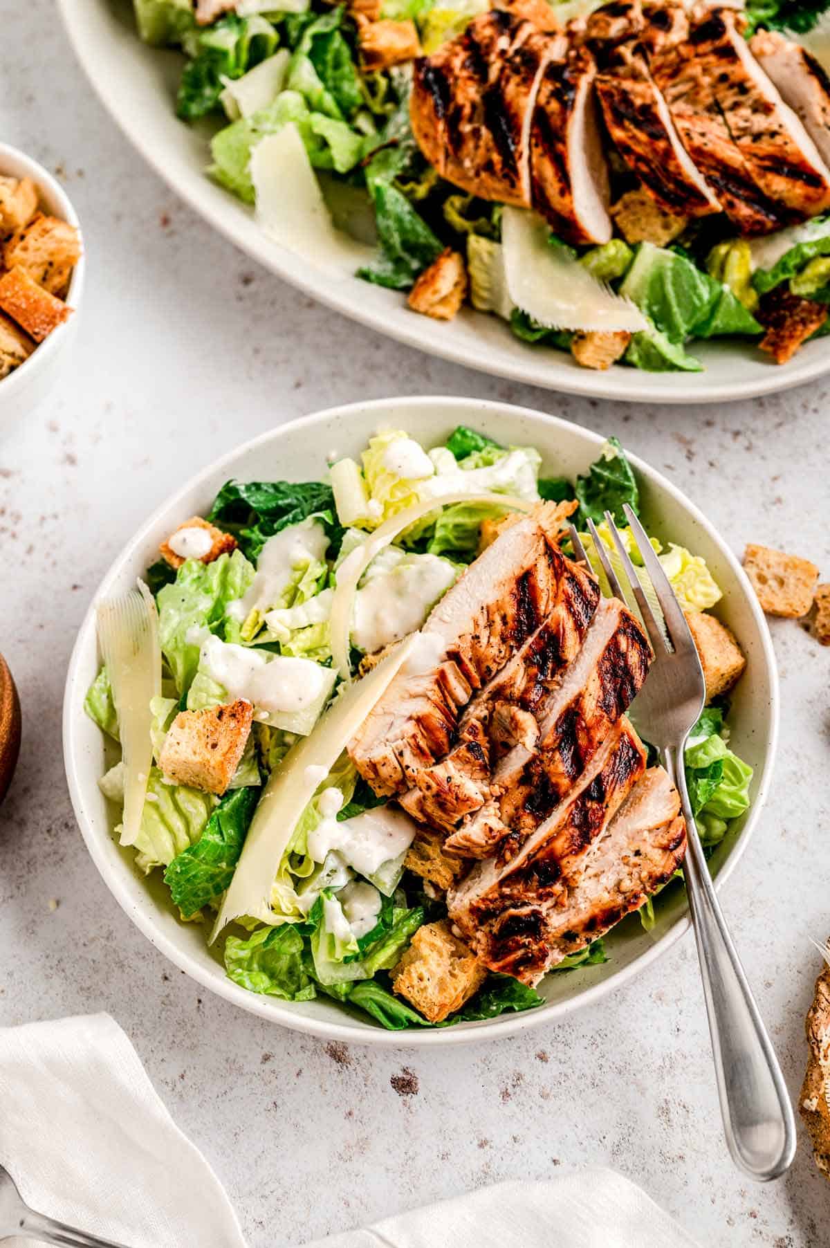 A bowl of healthy chicken caesar salad with a fork.