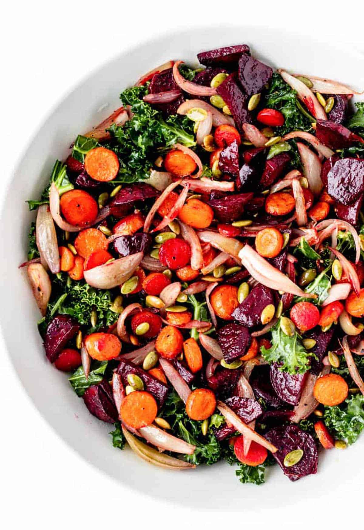 Bird's eye view of roasted beet and kale salad with carrots, shallots, pumpkin seeds and dried cranberries in a large bowl.