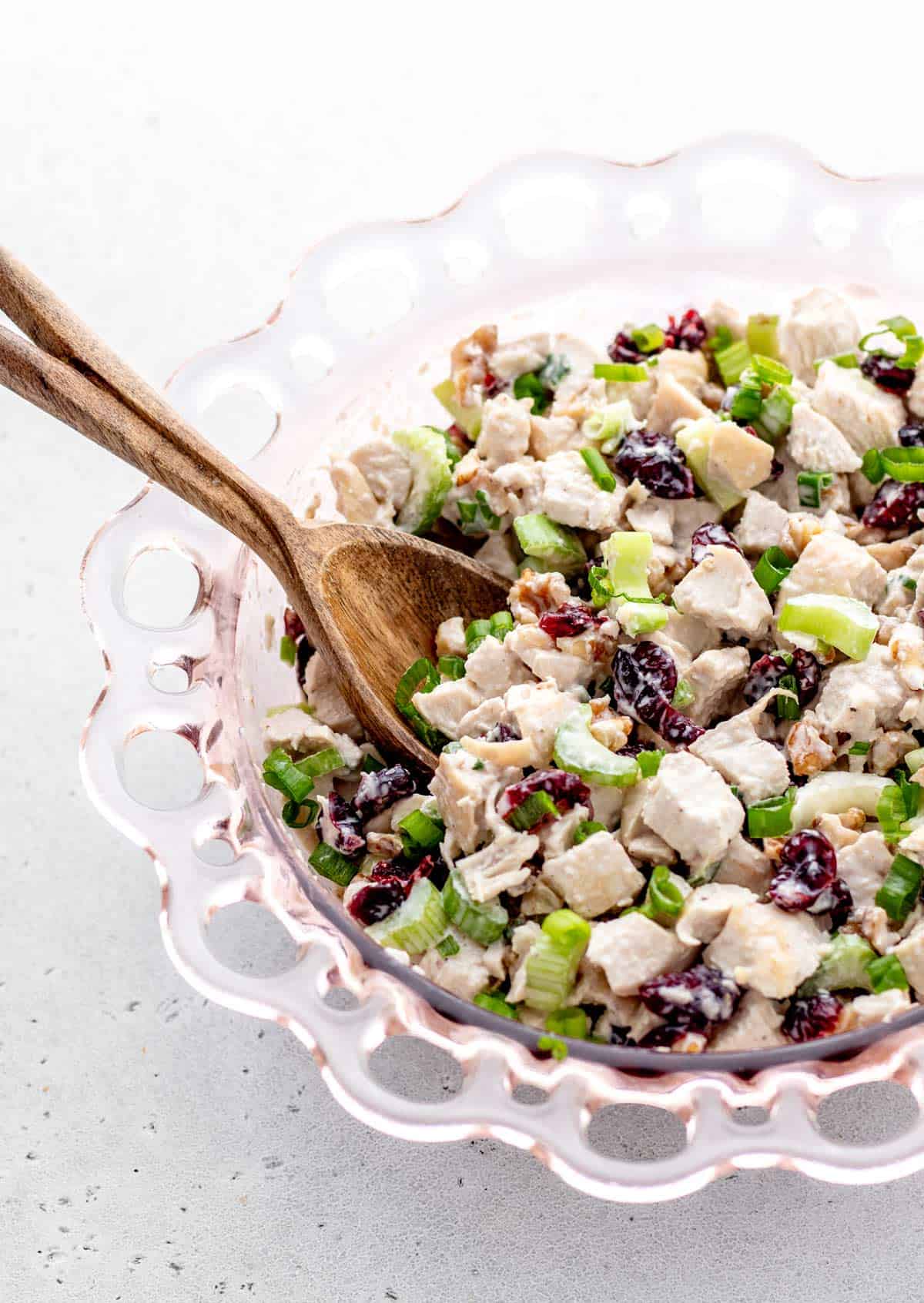 A wooden spoon scooping up some chicken salad with cranberries and walnuts.