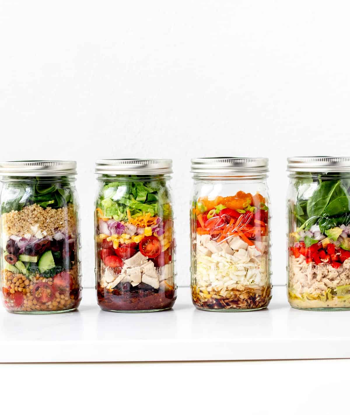 Four mason jar salads lined up in a row.