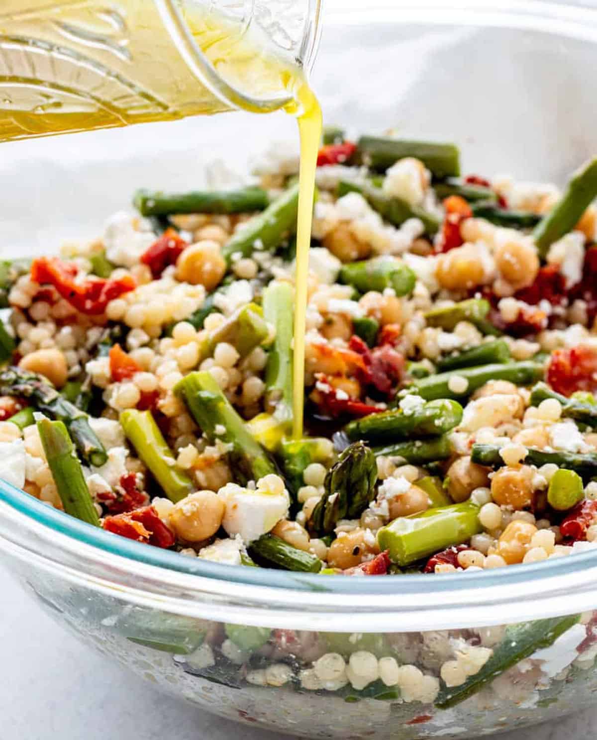 Dressing being poured over a bowl of asparagus couscous salad.