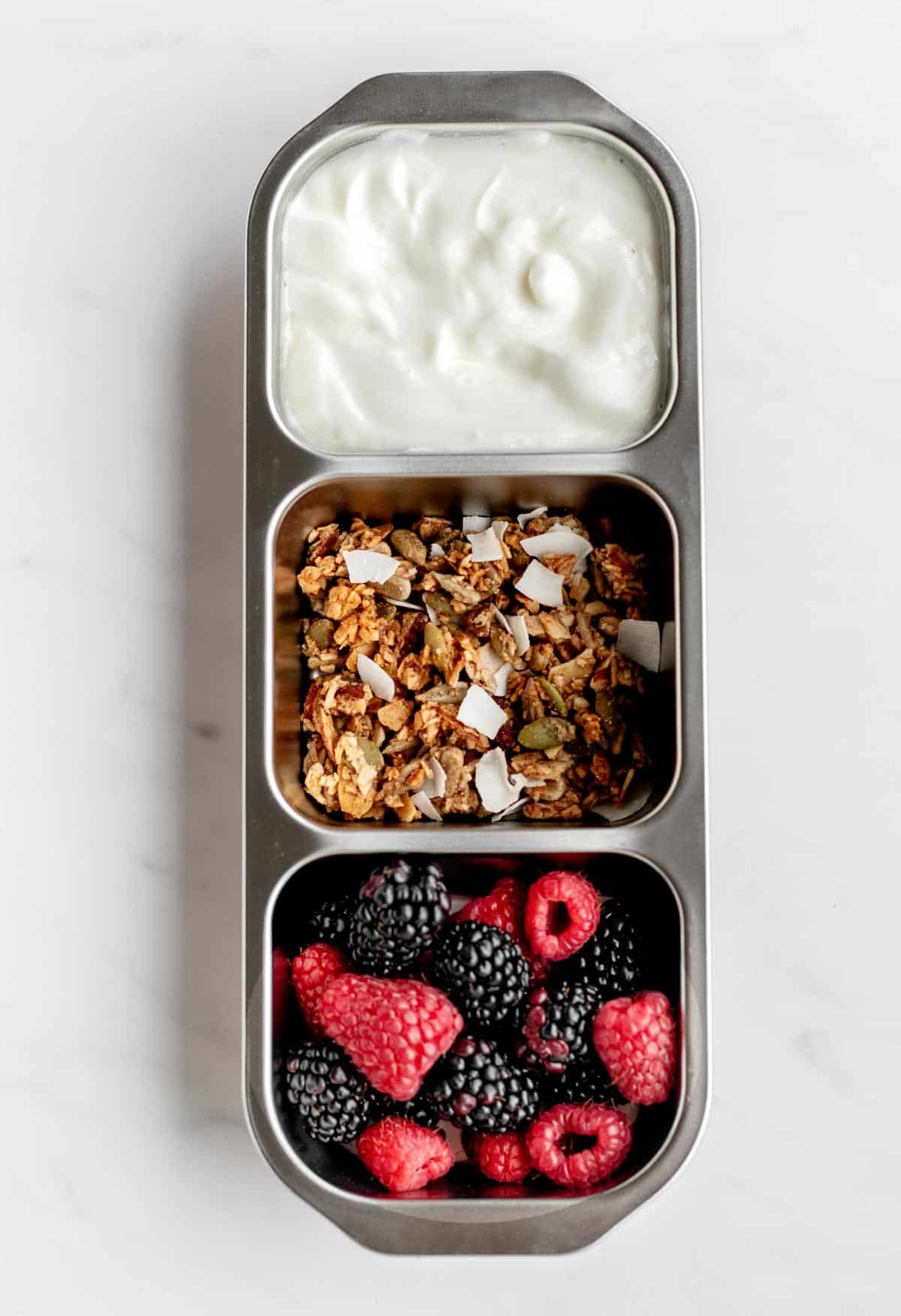 Bird's eye view of Greek yogurt, granola and mixed berries in a three compartment snack box.