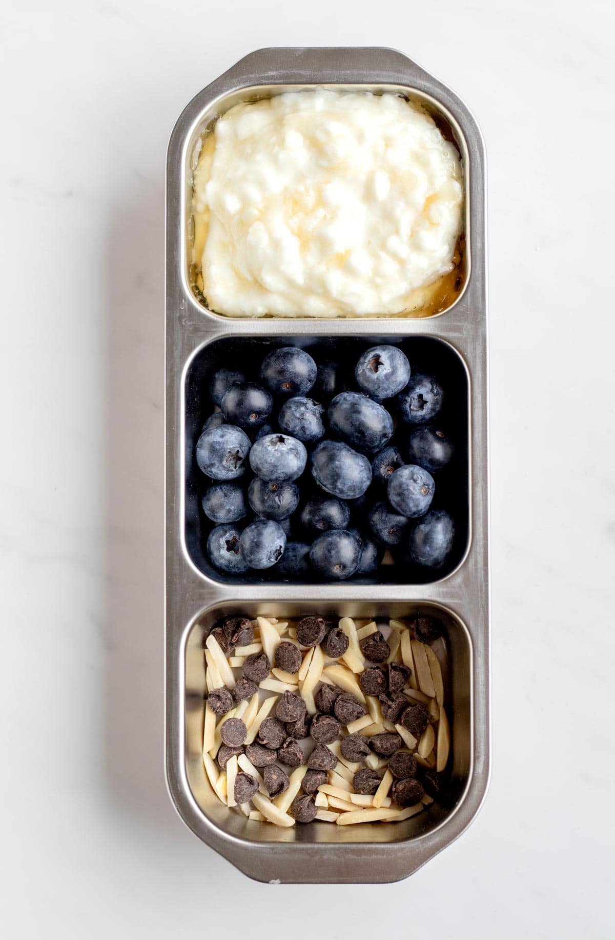 A snack box with cottage cheese, blueberries, slivered almonds and chocolate chips.