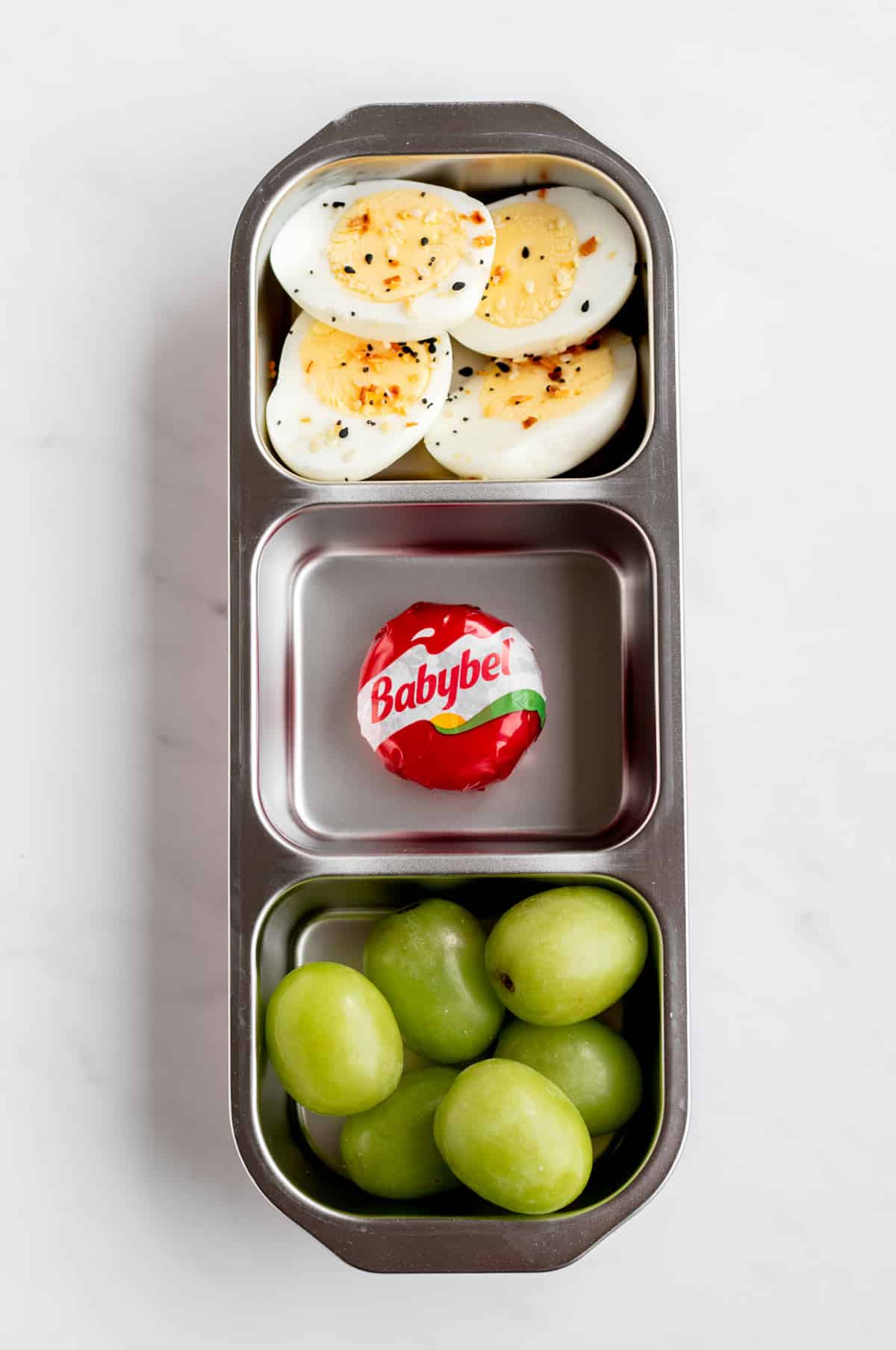 Four hard-boiled egg halves, a Babybel cheese and green grapes in a snack box.