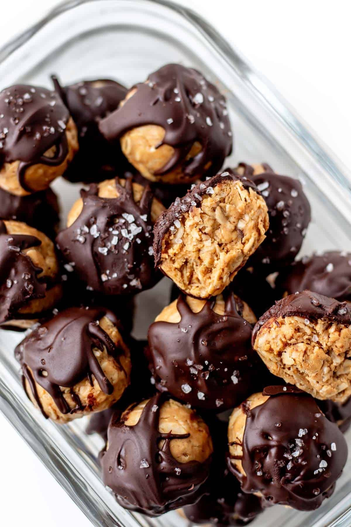 A chocolate peanut butter protein ball cut in half resting on a container with other bites.