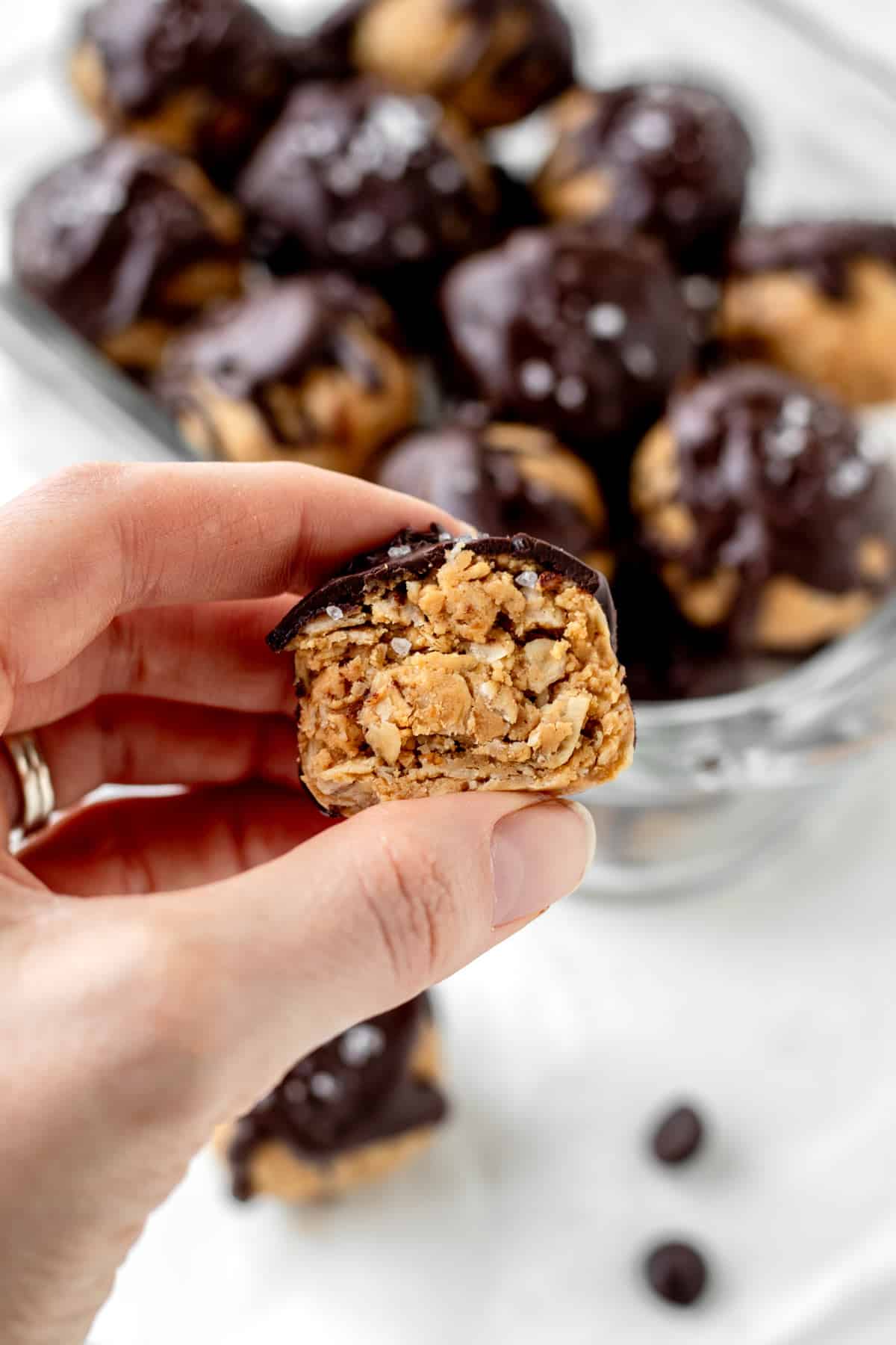 A hand holding a peanut butter protein balls that's cut in half.
