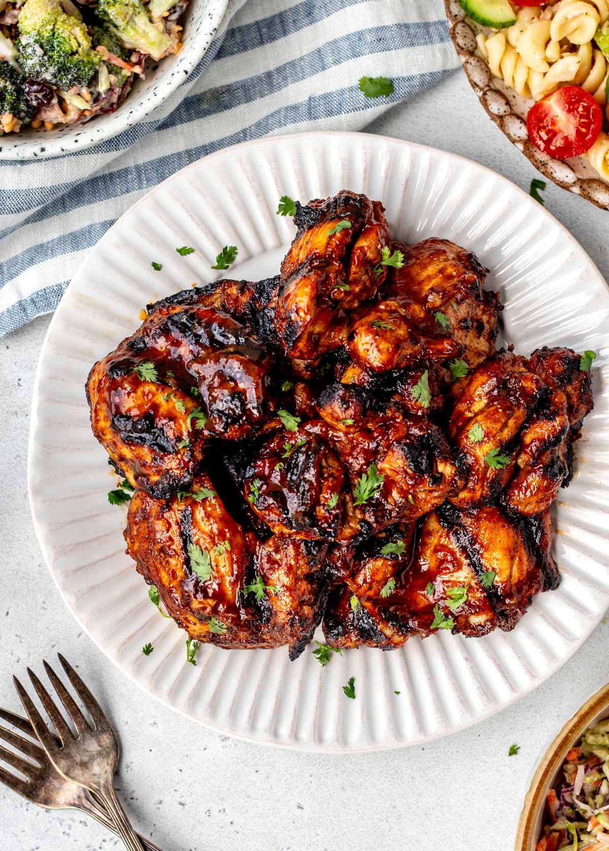 Bird's eye view of grilled BBQ boneless chicken thighs on a plate with some side salads.