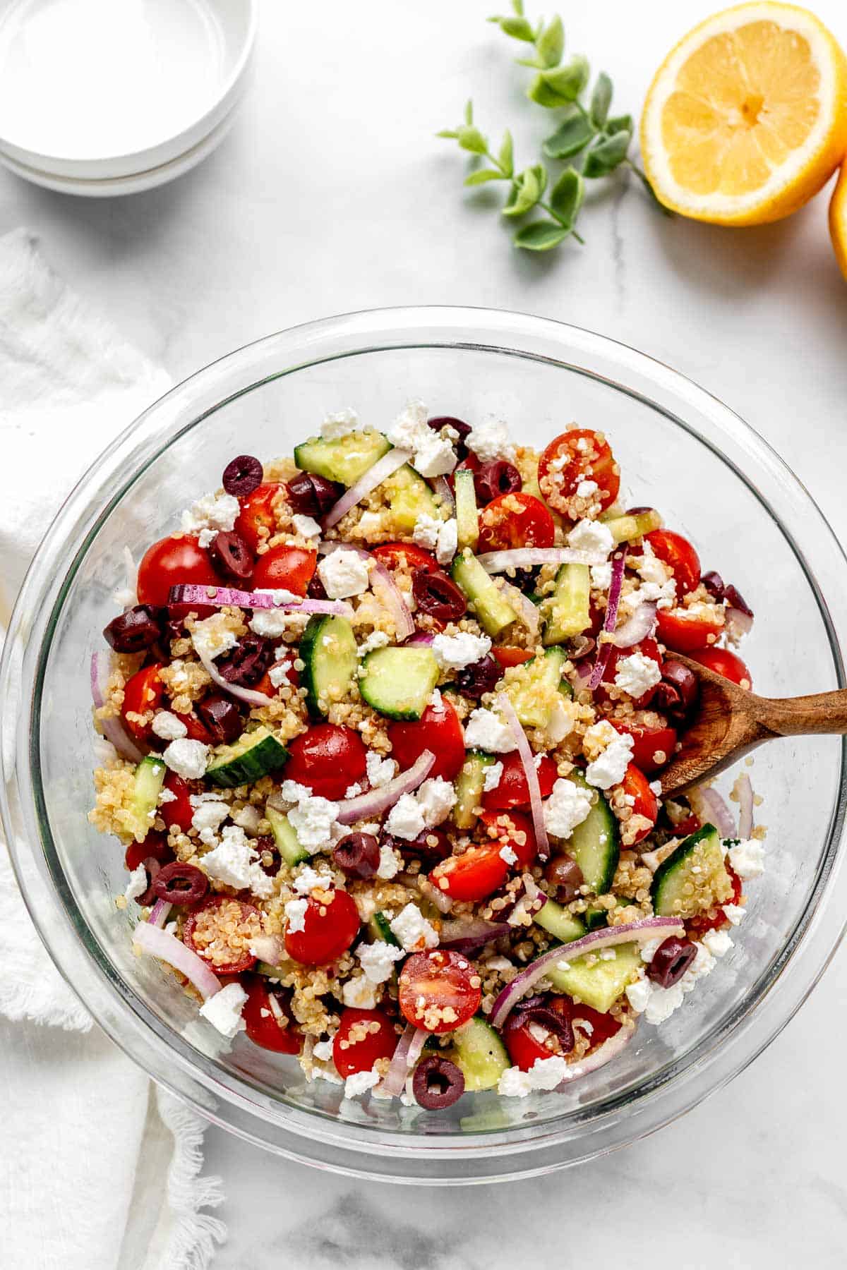 Bird's eye view of Greek quinoa salad in a large glass mixing bowl with a spoon in it.
