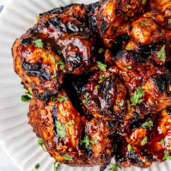 Close up bird's eye view of grilled bbq boneless chicken thighs stacked on a white plate.