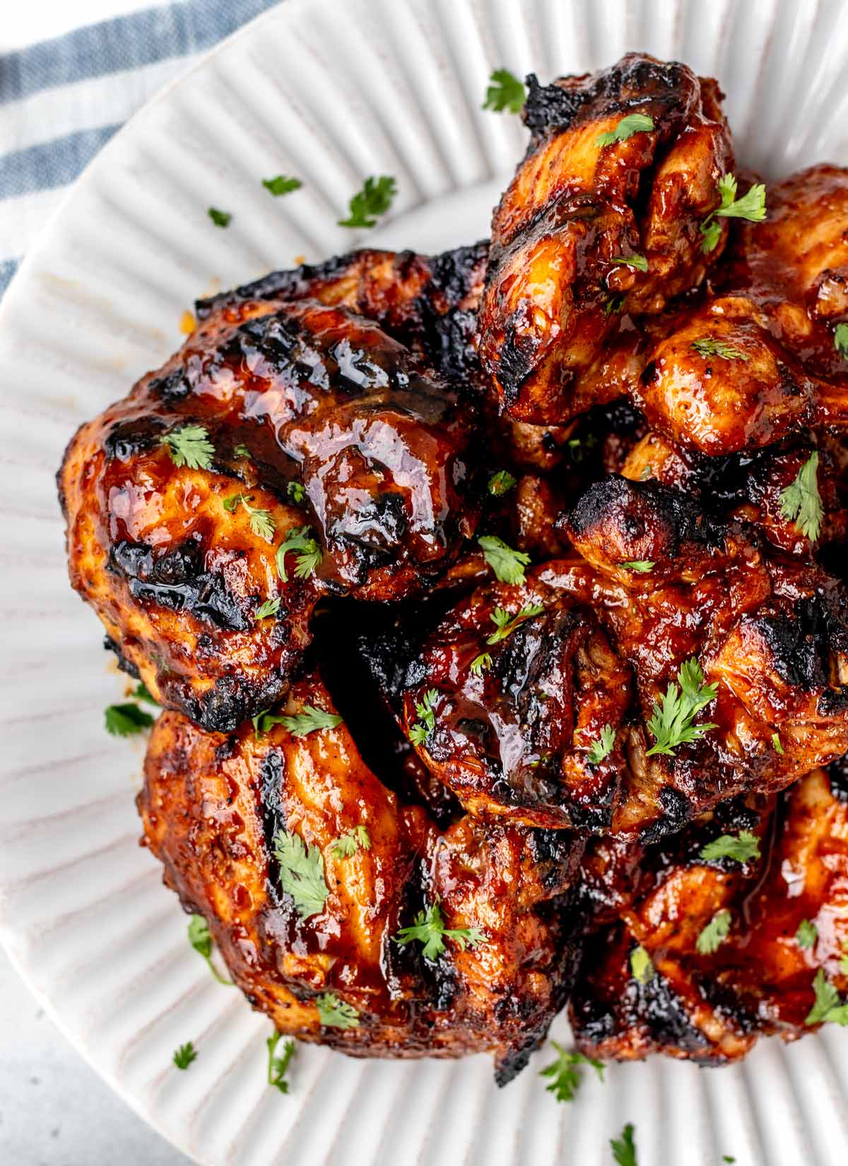 Bird's eye view of grilled BBQ chicken thighs on a white plate topped with parsley.