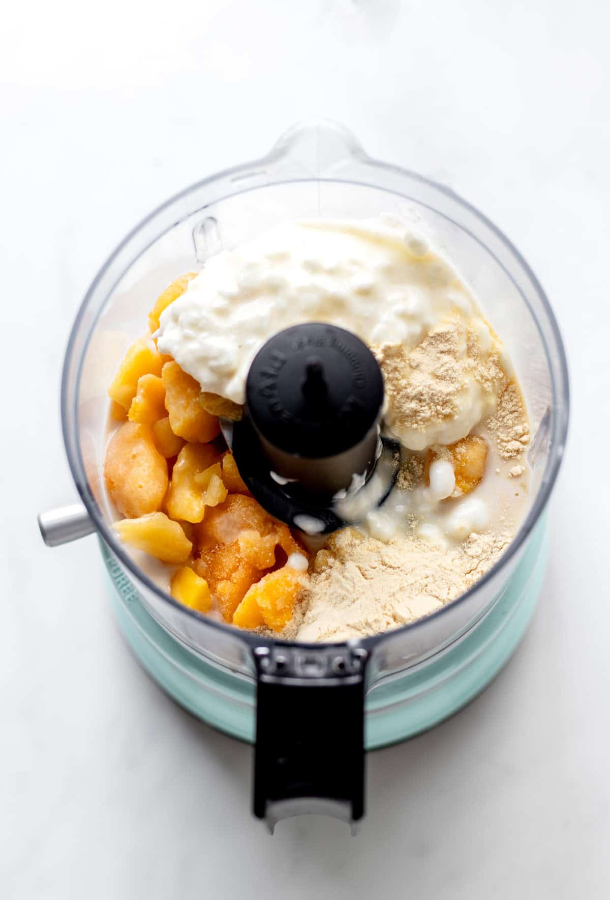 Ingredients for protein mango dole whip in a mini food processor.