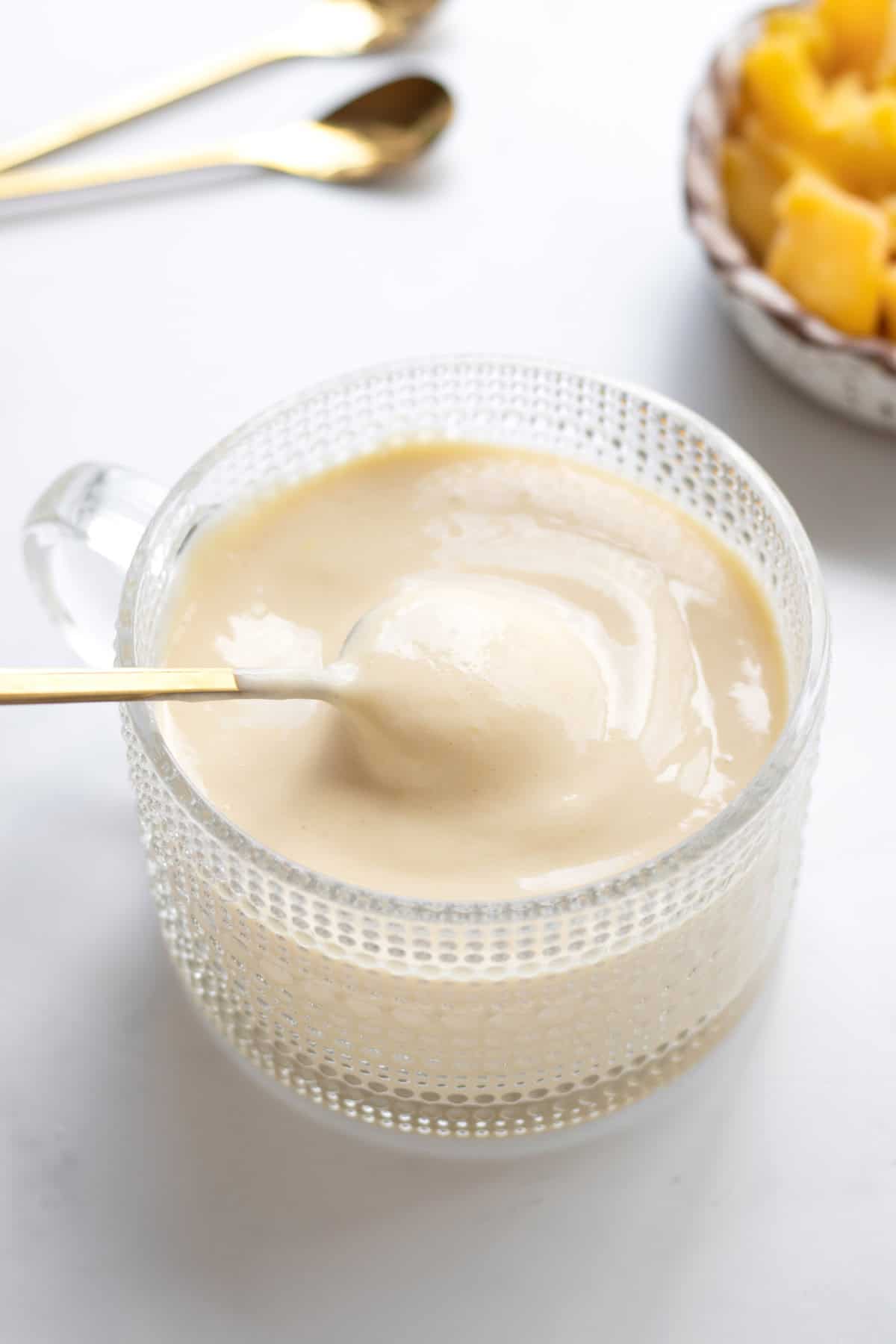 A gold spoon scooping up some of the mango whip in a glass cup.