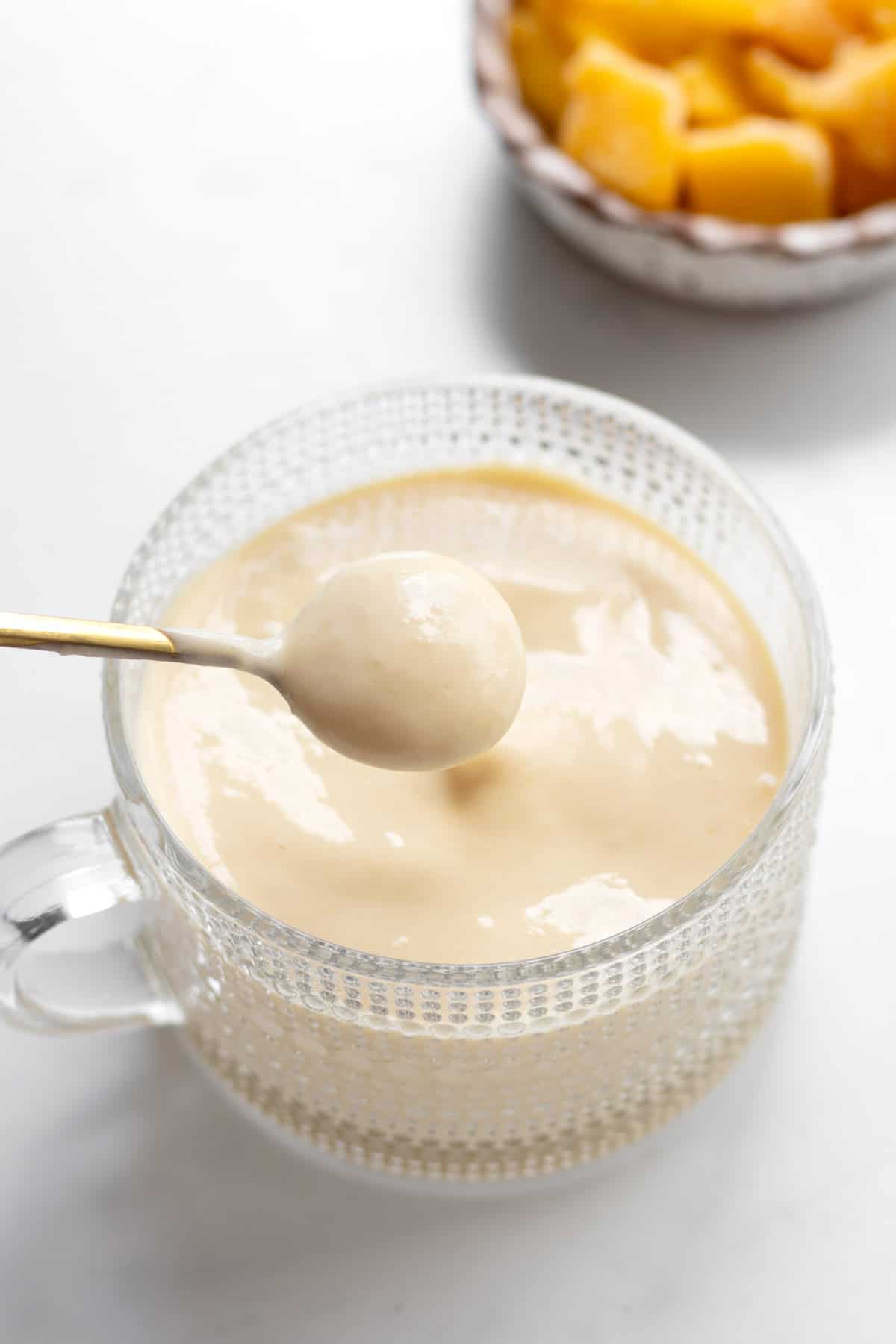A spoon scooping up some of the protein mango whip from a glass cup.