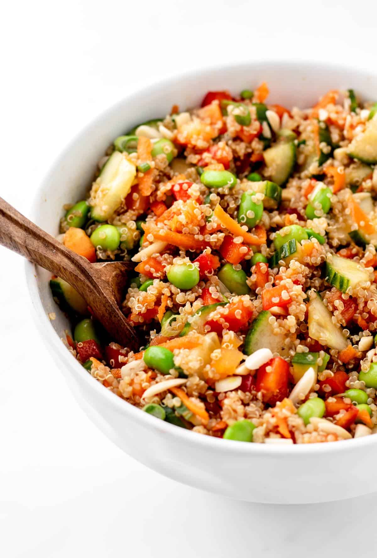 A wooden spoon digging into Asian edamame quinoa salad with a sesame dressing.