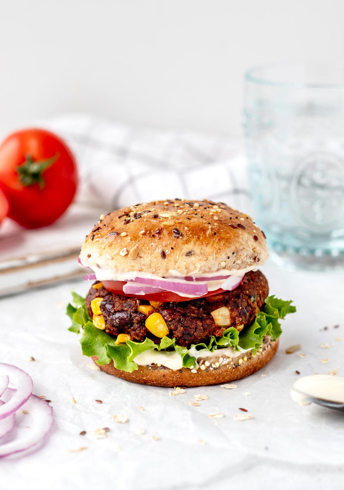 A spicy bean burger on a bun with toppings next to a glass.