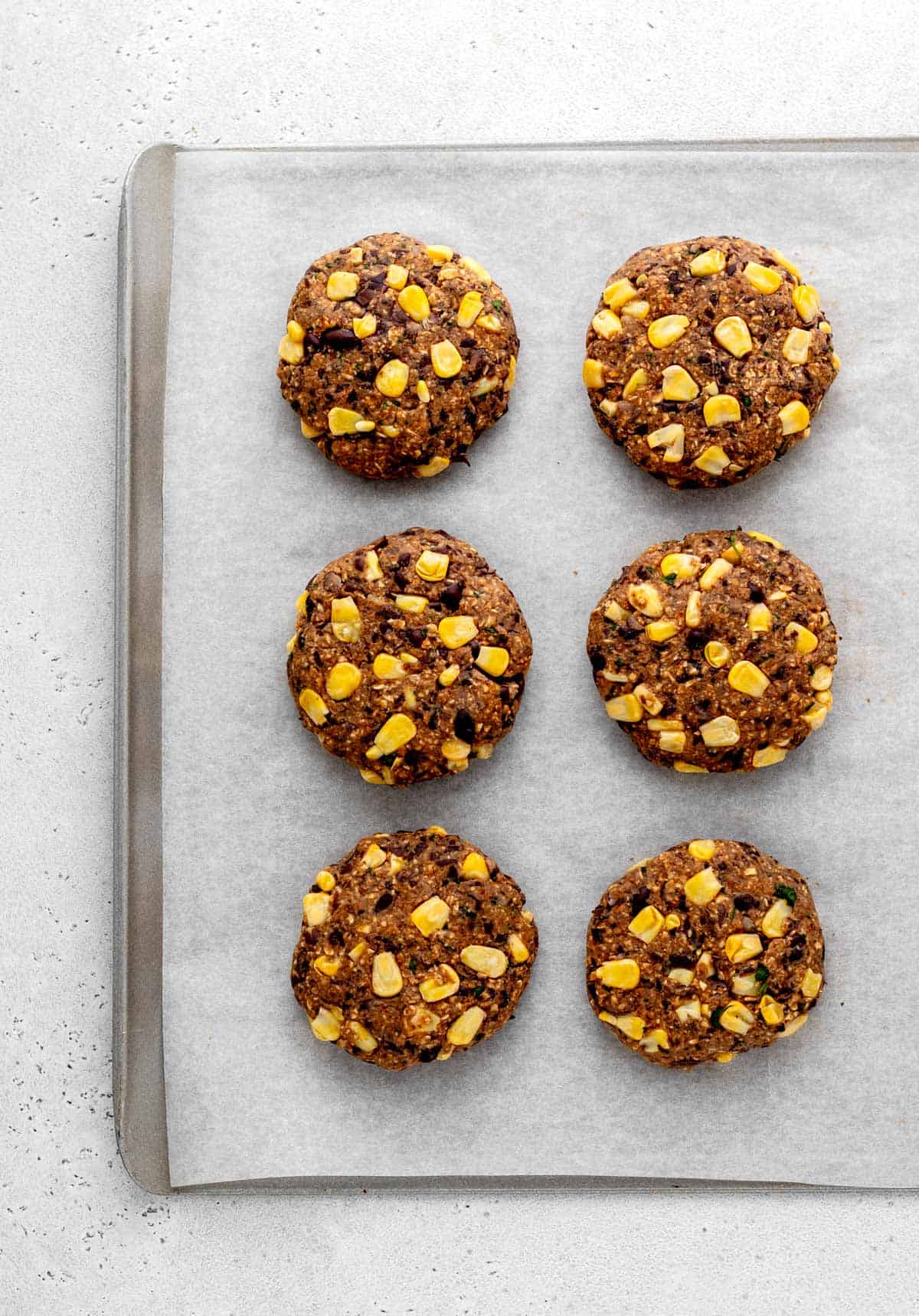 Six uncooked bean burgers on a baking sheet.