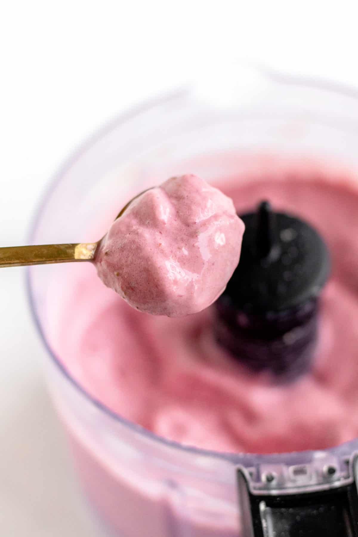 A gold spoon holding up some of the strawberry and cottage cheese dessert.