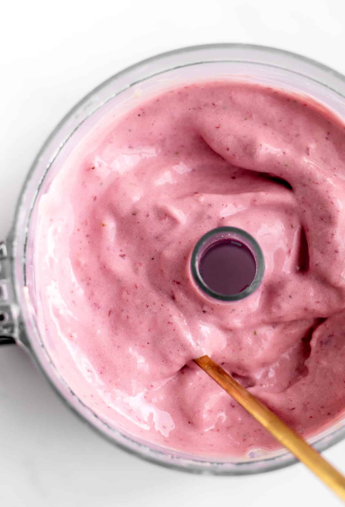 Bird's eye view of a gold spoon in a mini food processor with cottage cheese strawberry dessert.