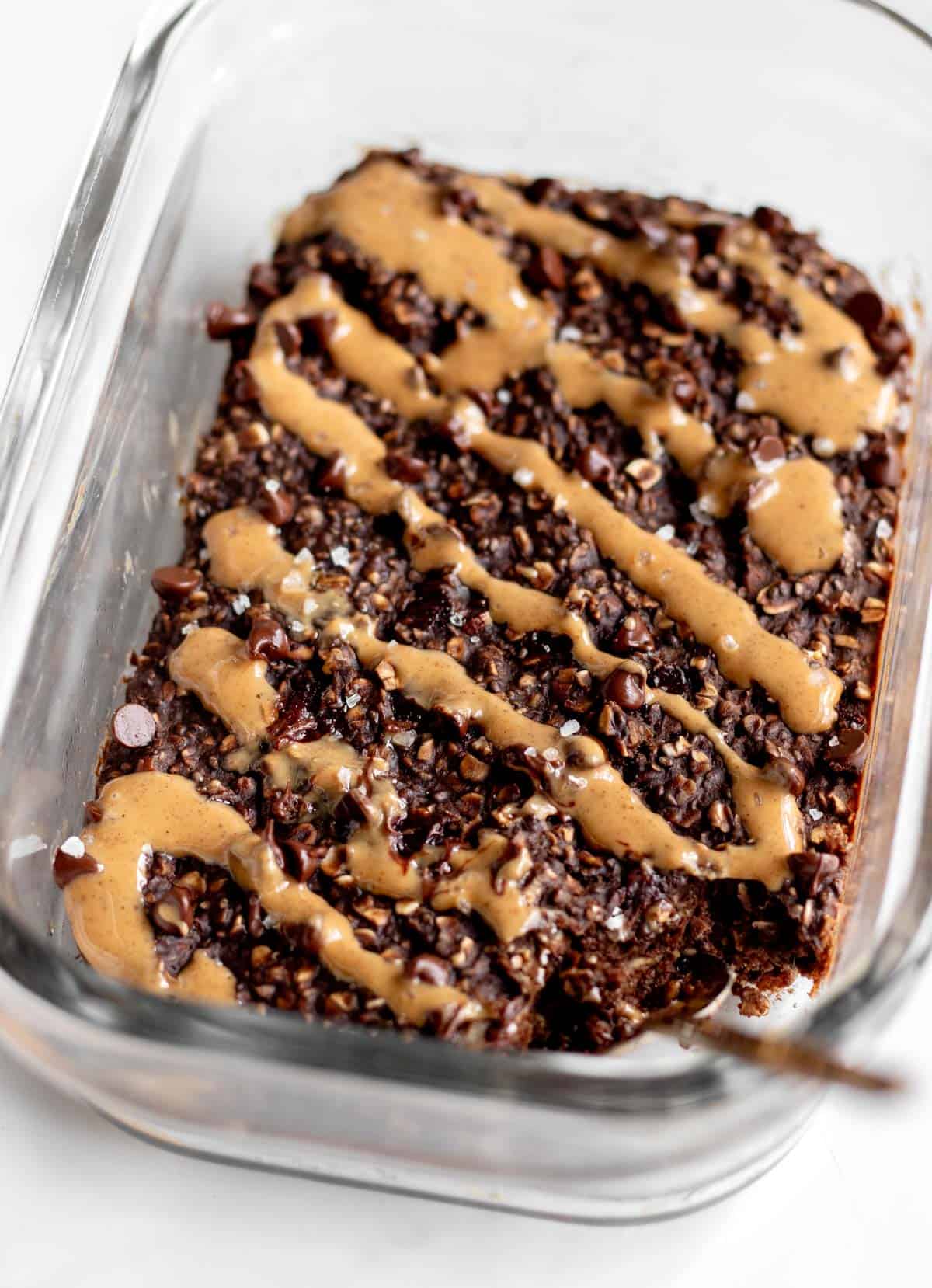 A spoon digging into a glass container of protein baked oats drizzled with peanut butter.