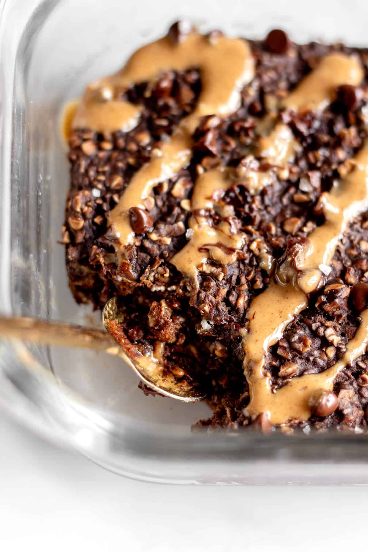 A spoon digging into the chocolate protein baked oats in a glass dish.
